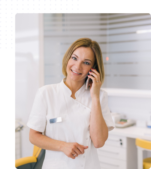 Secrétaire dentaire en blouse blanche parlant au téléphone dans un cabinet dentaire, représentant le rôle d’accueil et de coordination auprès des patients et du praticien.