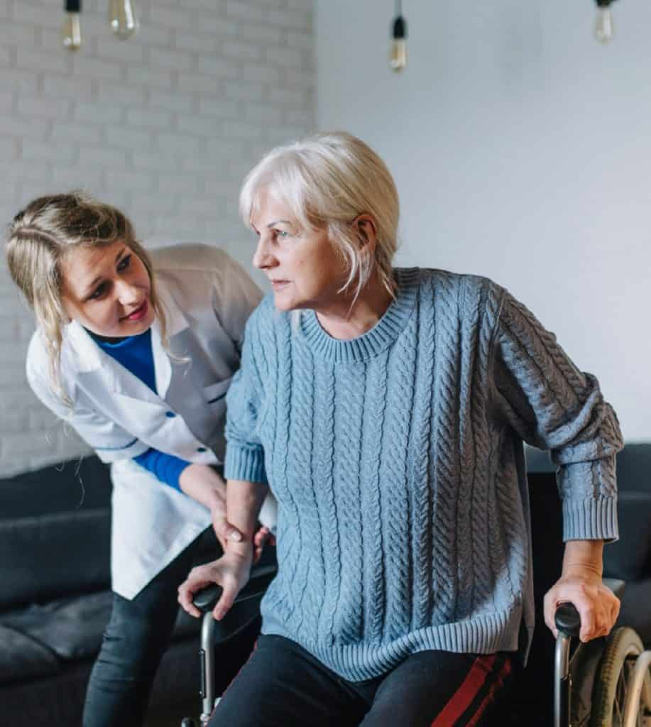 soignante avec personne âgée se relevant de son fauteuil roulant