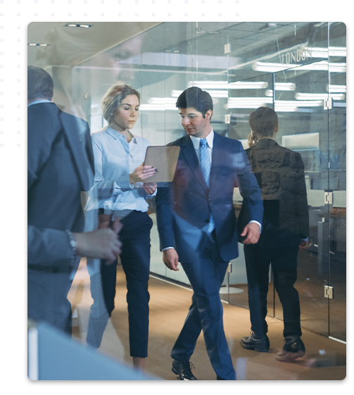Deux fonctionnaires en tenue de travail formelle marchent et discutent dans un bureau moderne avec des parois en verre, l’homme en costume bleu et la femme en chemisier bleu ciel tenant un dossier.