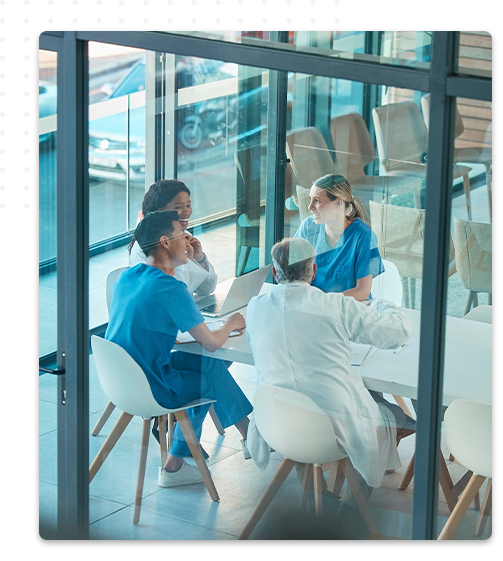 Un groupe de professionnels de santé en uniformes bleus et blancs réunis autour d'une table en discussion, vue à travers une vitre dans un cadre de bureau moderne et lumineux.