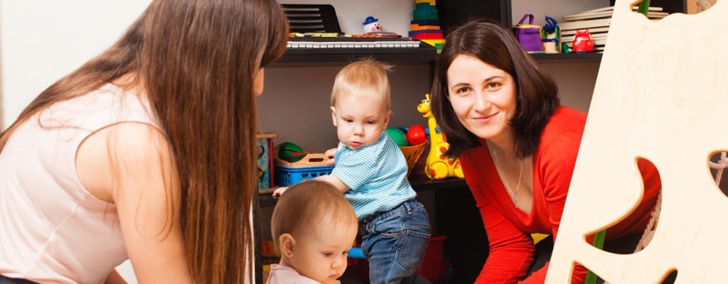 une agent petite enfance souriante au milieu de jeunes enfants